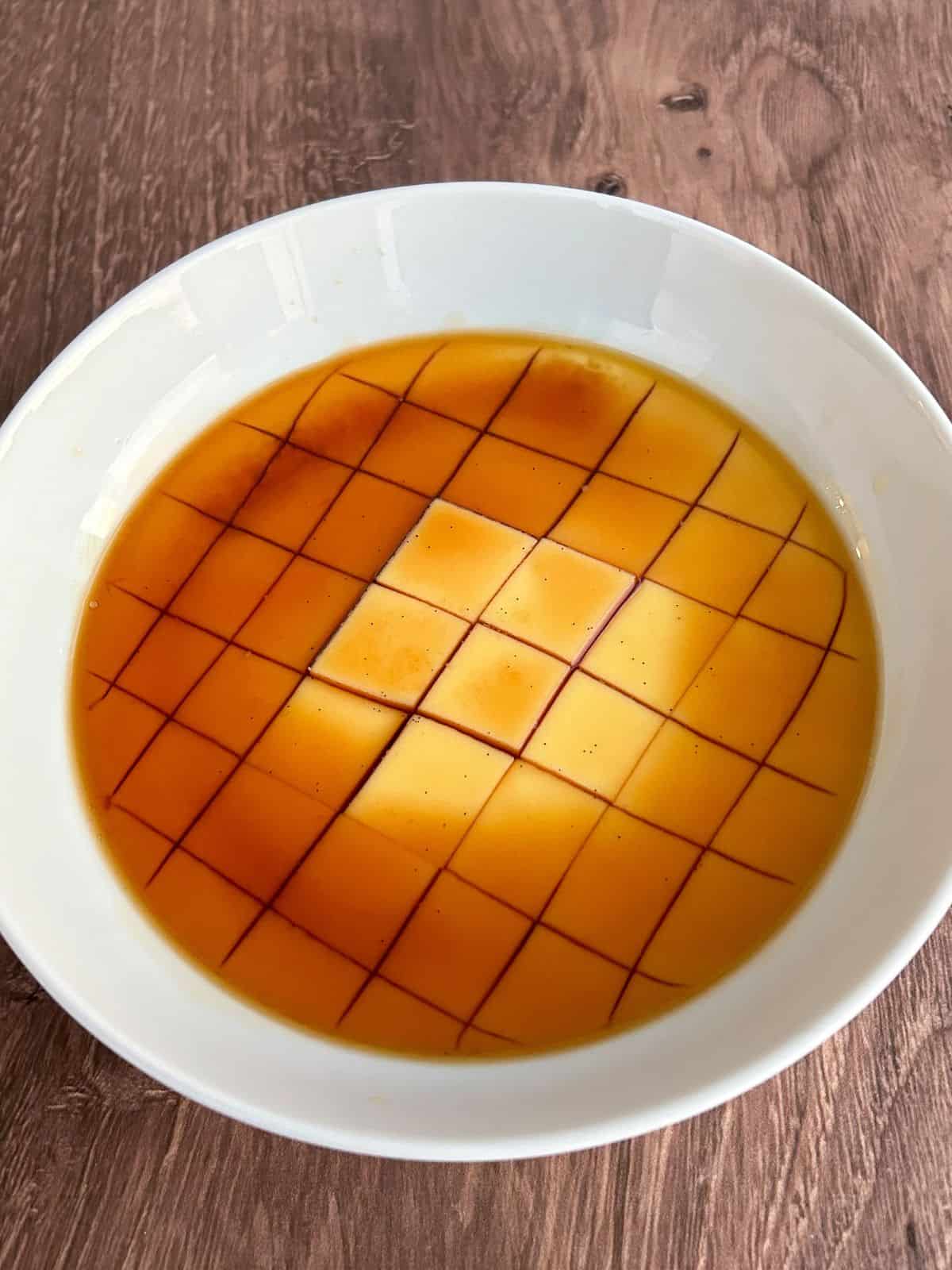 Microwave flan in a bowl sliced into cubes and topped with caramel.
