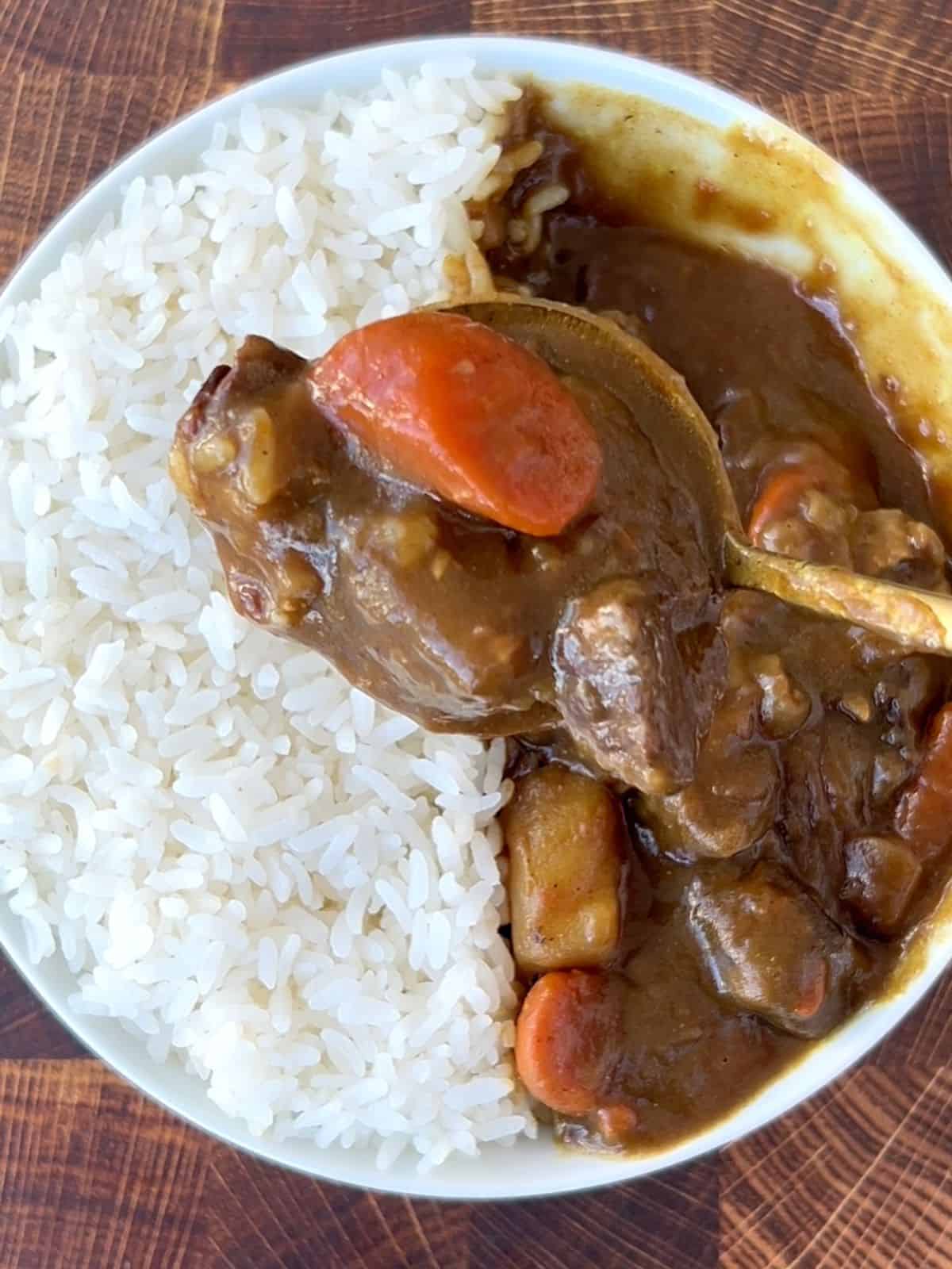 Spoonful of Japanese beef curry with the bowl of curry and rice underneath it.