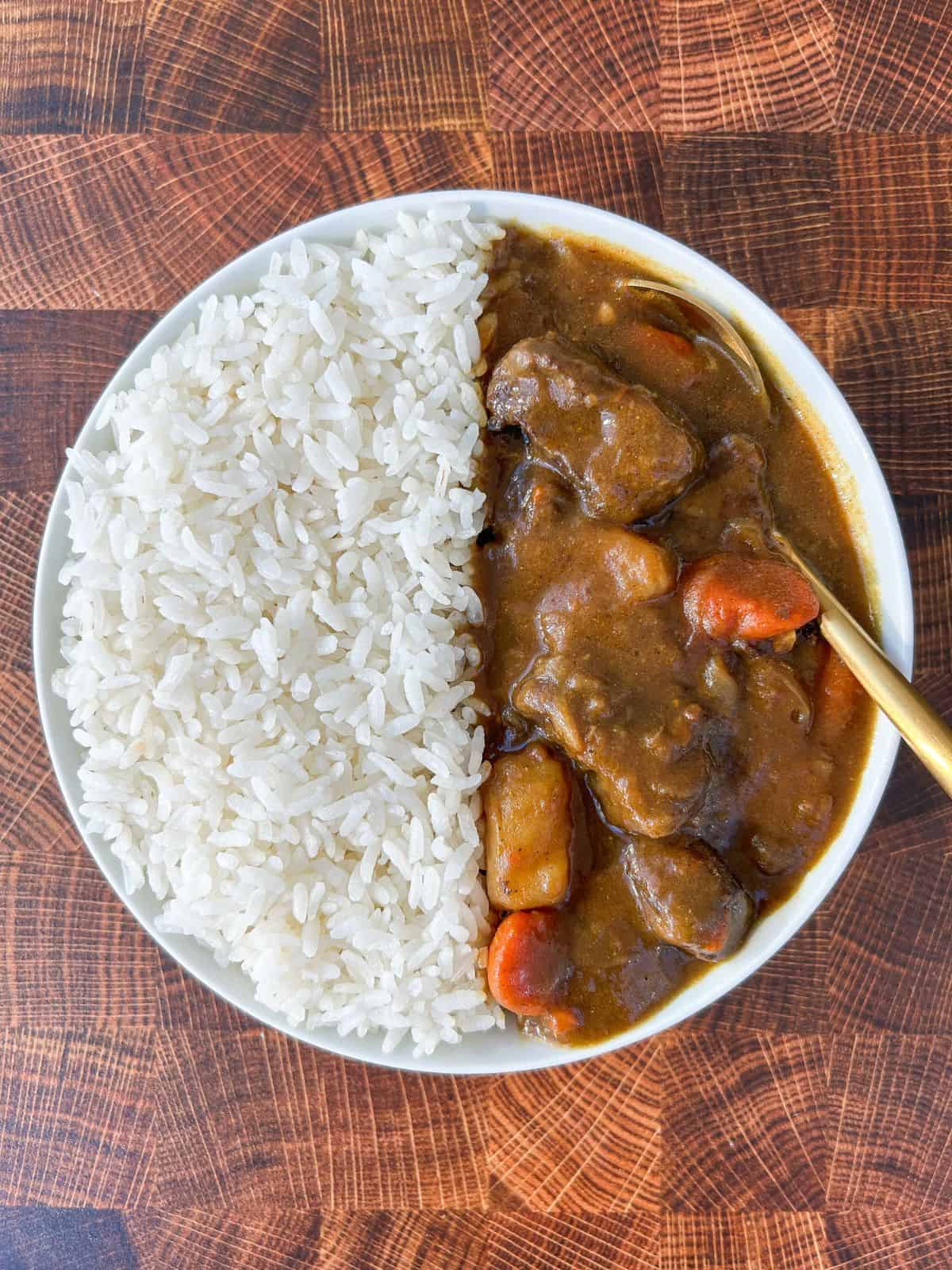 Bowl filled with half rice, half Japanese beef curry with a spoon in it.