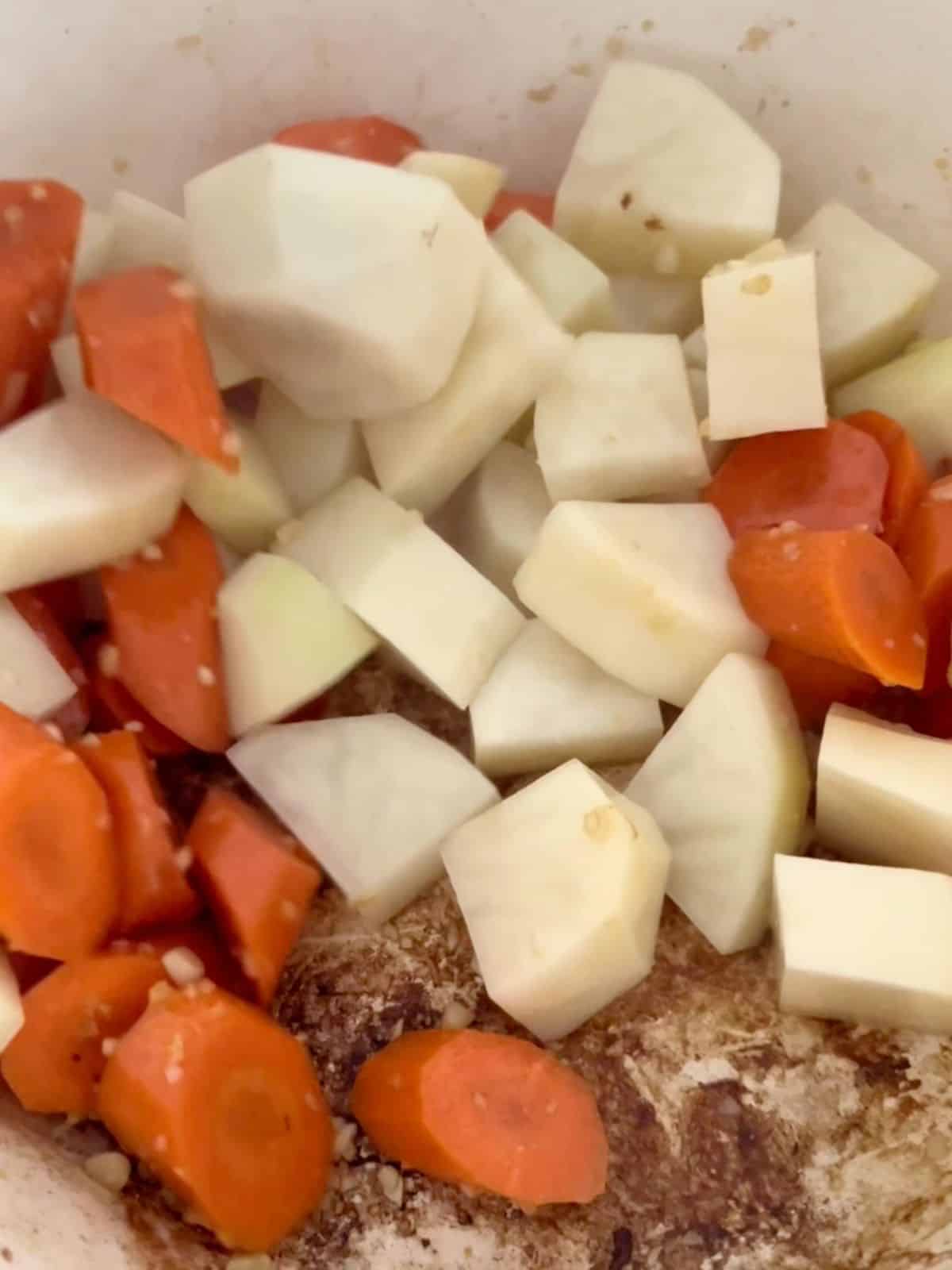 Carrots and potatoes with garlic being cooked in a Dutch oven.