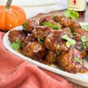 Sweet chili cocktail meatballs on a serving platter garnished with scallions and cilantro.
