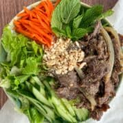 Overhead shot of Vietnamese lemongrass beef served with vegetables, herbs, and peanuts on a bed of noodles.