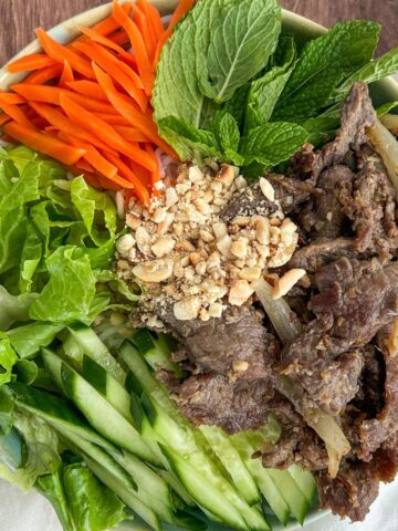 Overhead shot of Vietnamese lemongrass beef served with vegetables, herbs, and peanuts on a bed of noodles.