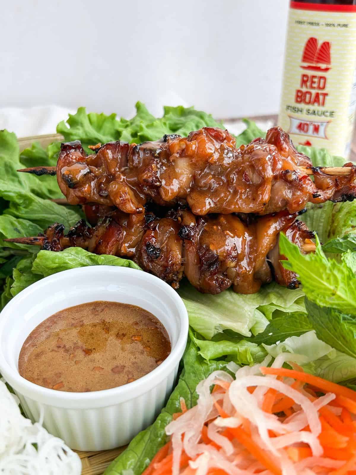 Hot honey glazed chicken skewers on a bed of lettuce with a side of sauce next to it.