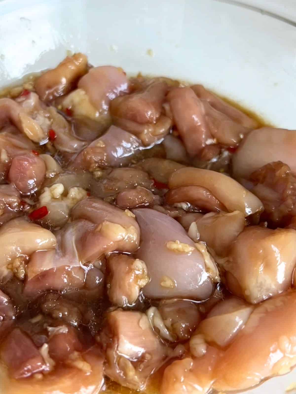 Diced chicken thighs marinating in a glass bowl.