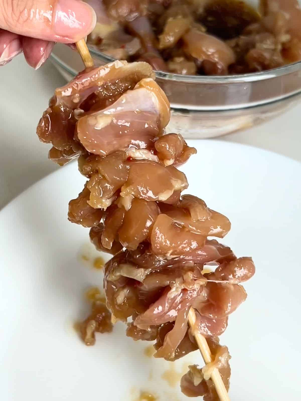 Raw chicken pieces skewered on a wooden skewer.