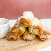 A side shot of the egg rolls stacked on top of each other and garnished with shaved Parmesan cheese.