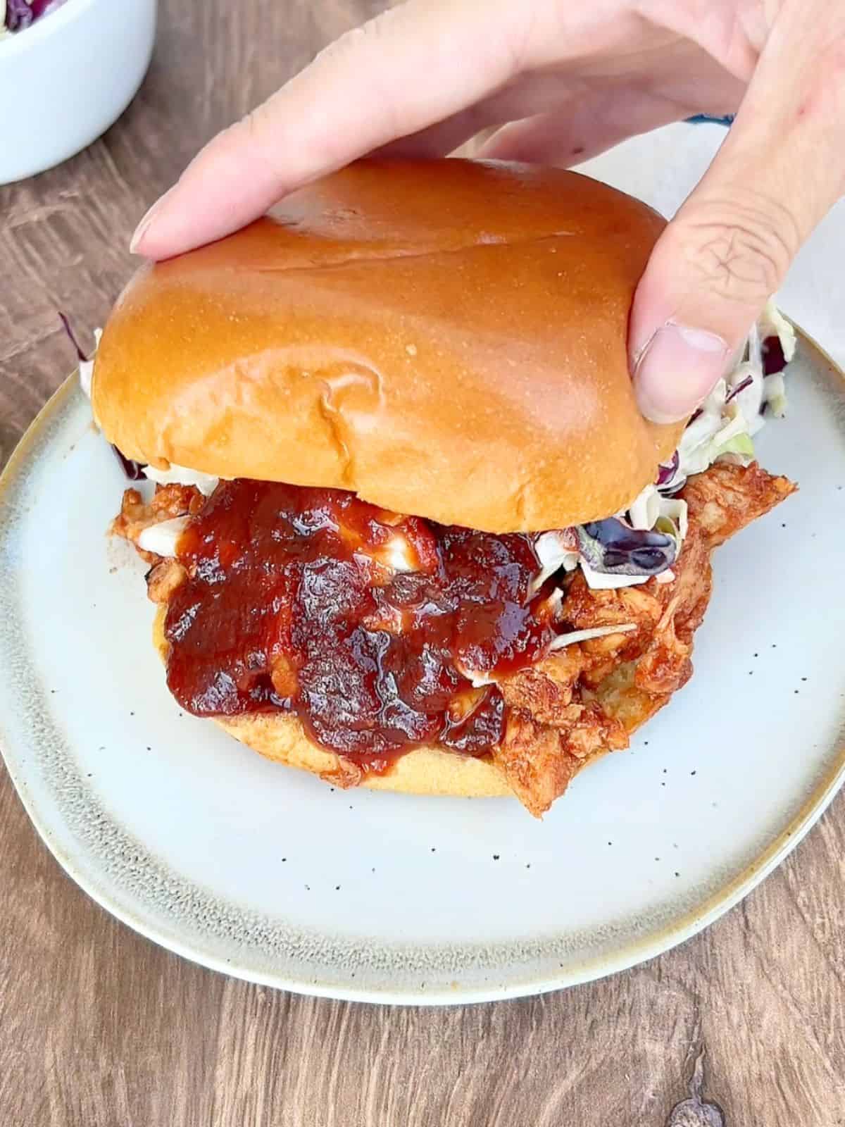 Hand assembling the BBQ tuna sandwich and putting the top bun on top.