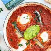 Sardine shakshuka in a skillet garnished with avocado and parsley.