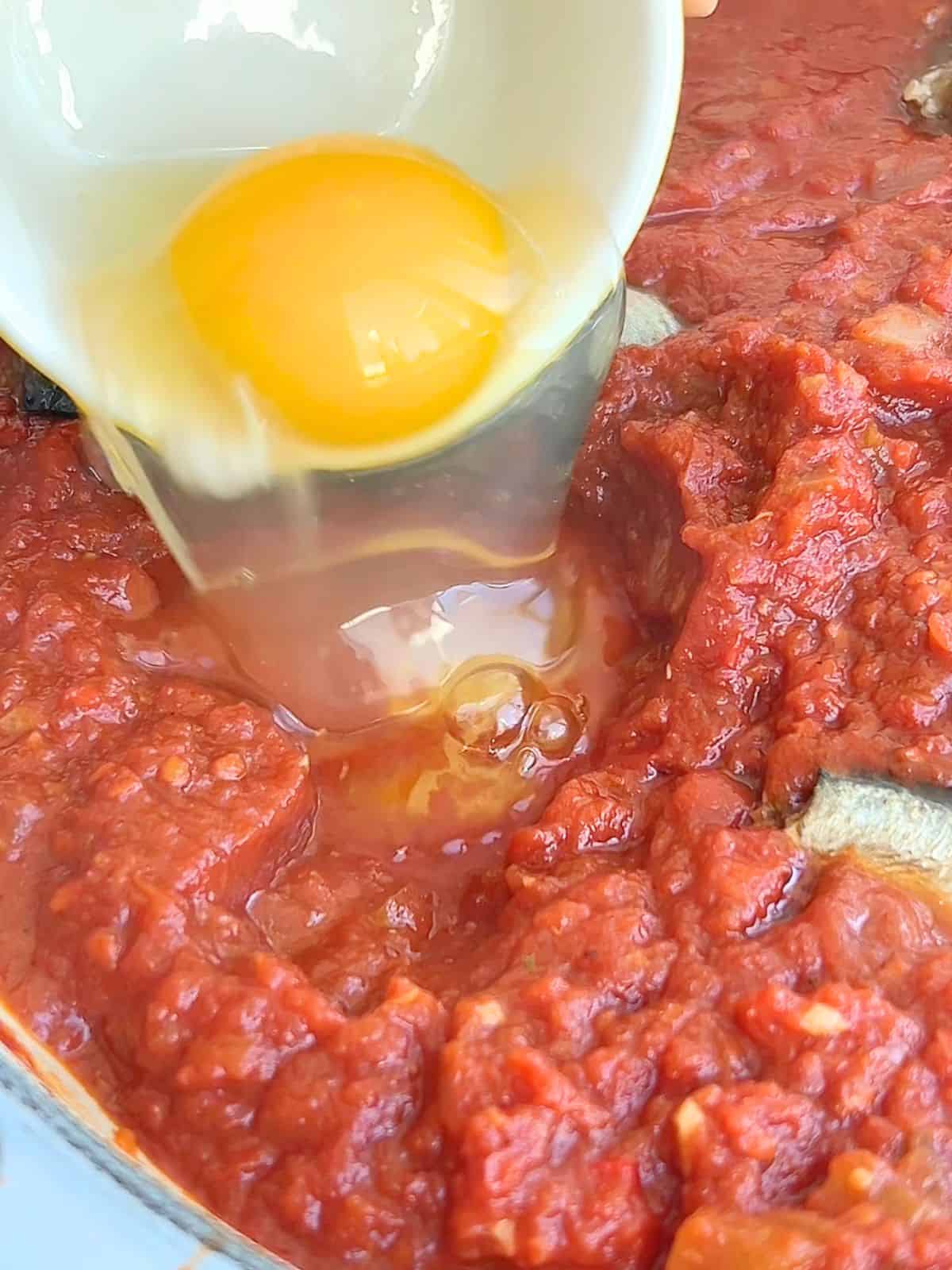 Adding the sardines and eggs to the shakshuka in a skillet.