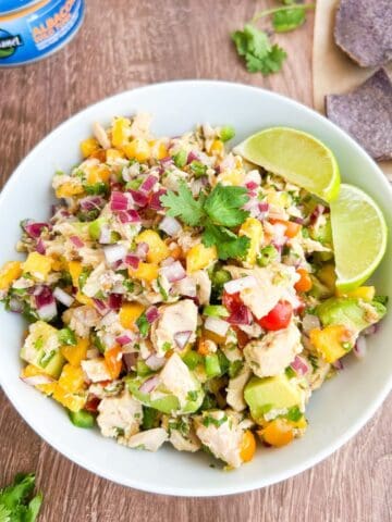 Mango tuna ceviche served in a white bowl with a side of lime wedges.