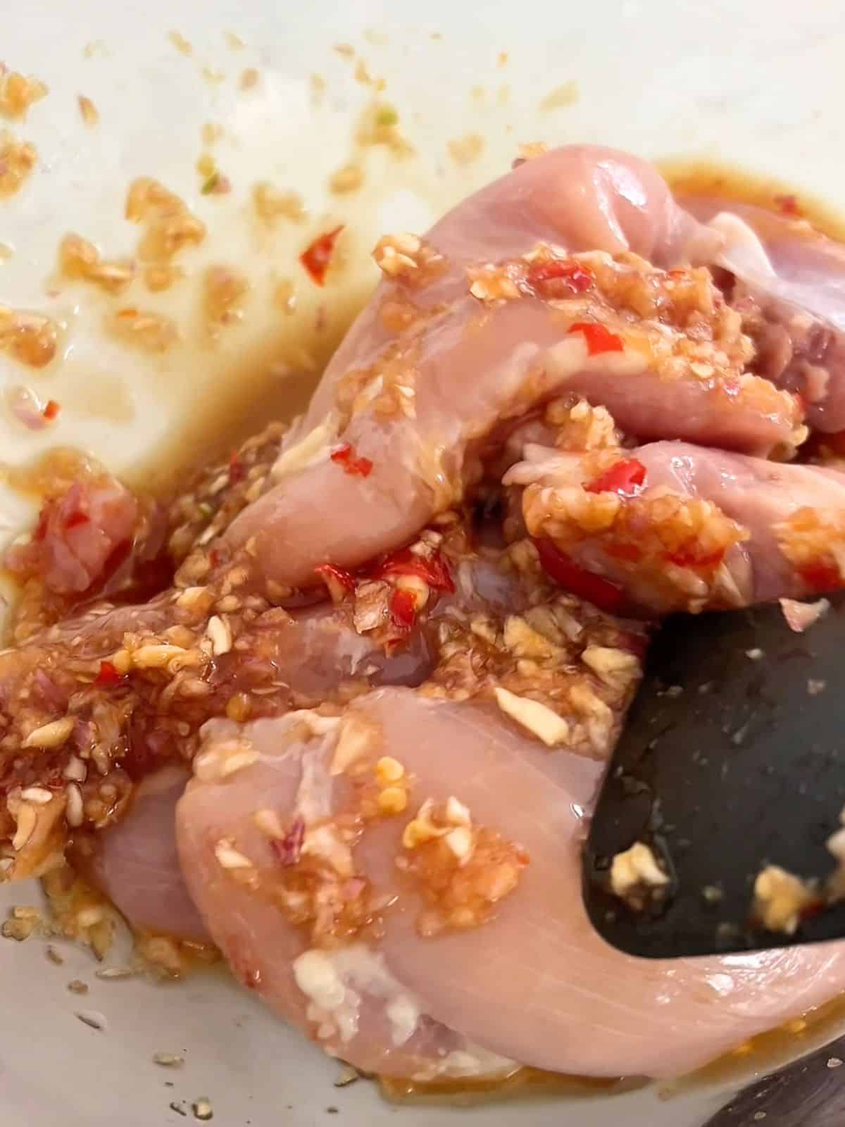 Chicken thighs in a glass mixing bowl in a fish sauce marinade.