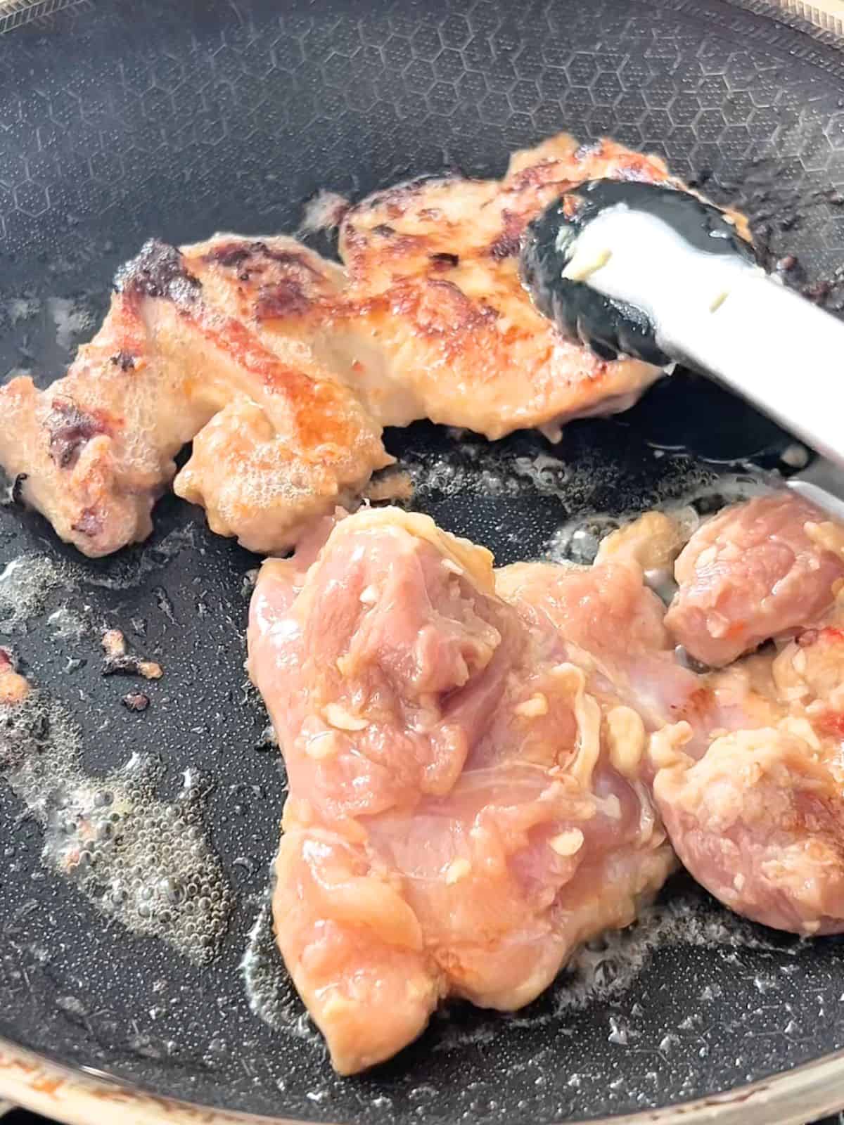 Cooking the marinated chicken thighs in a skillet.