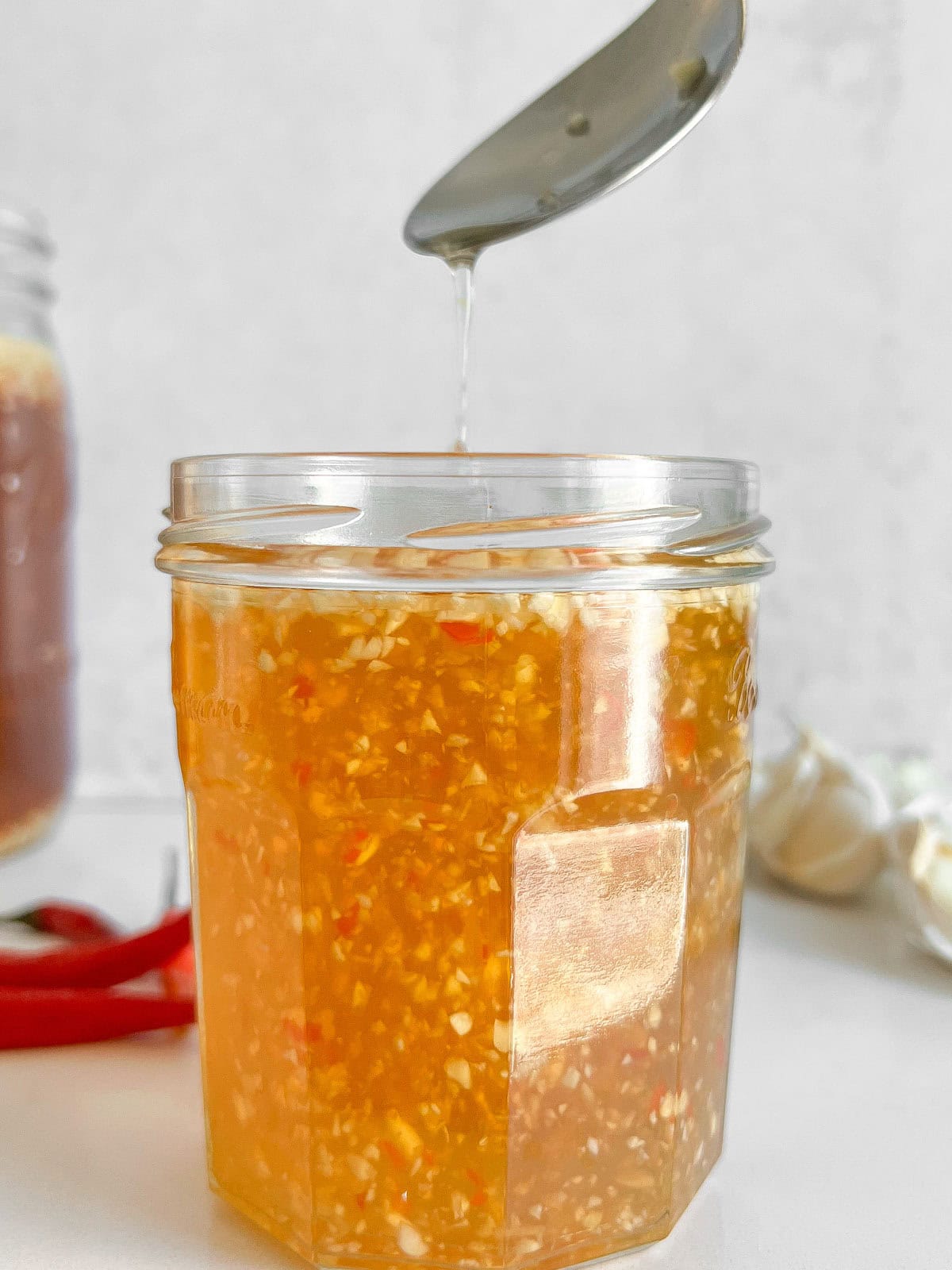 Fish sauce being poured into a jar with a spoon.