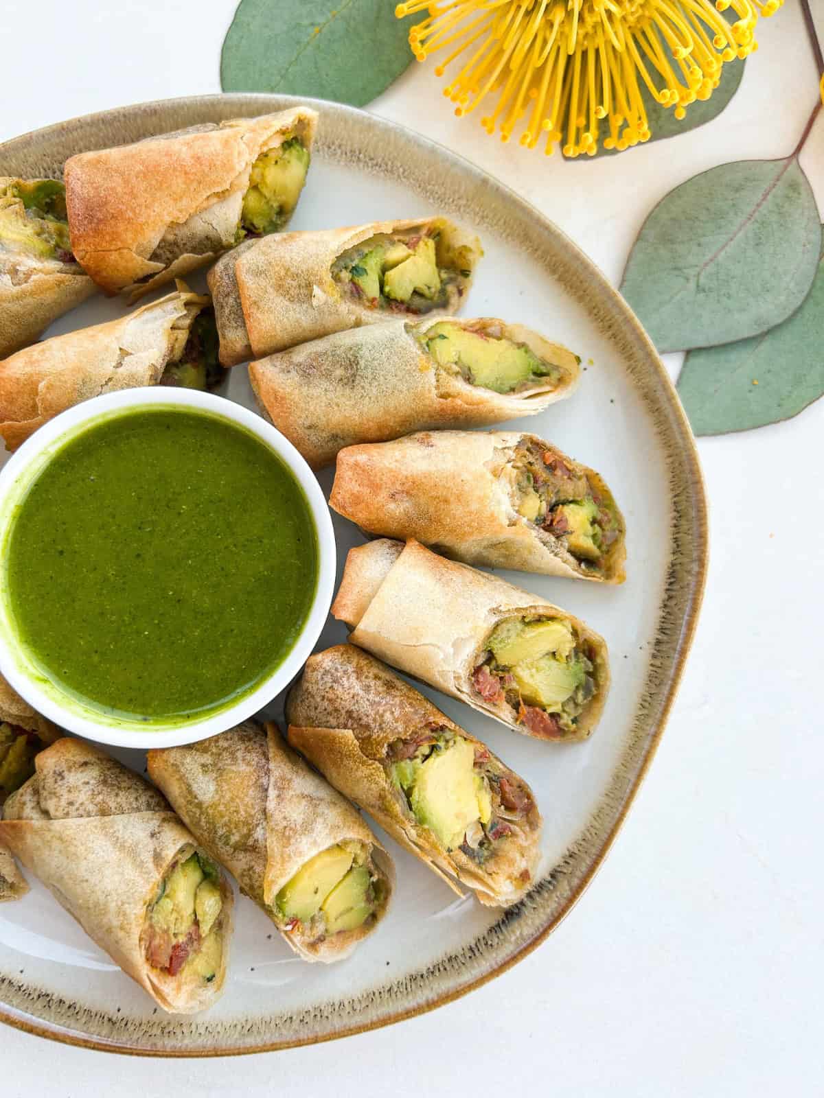 Avocado egg rolls served on a serving dish with a green dipping sauce.