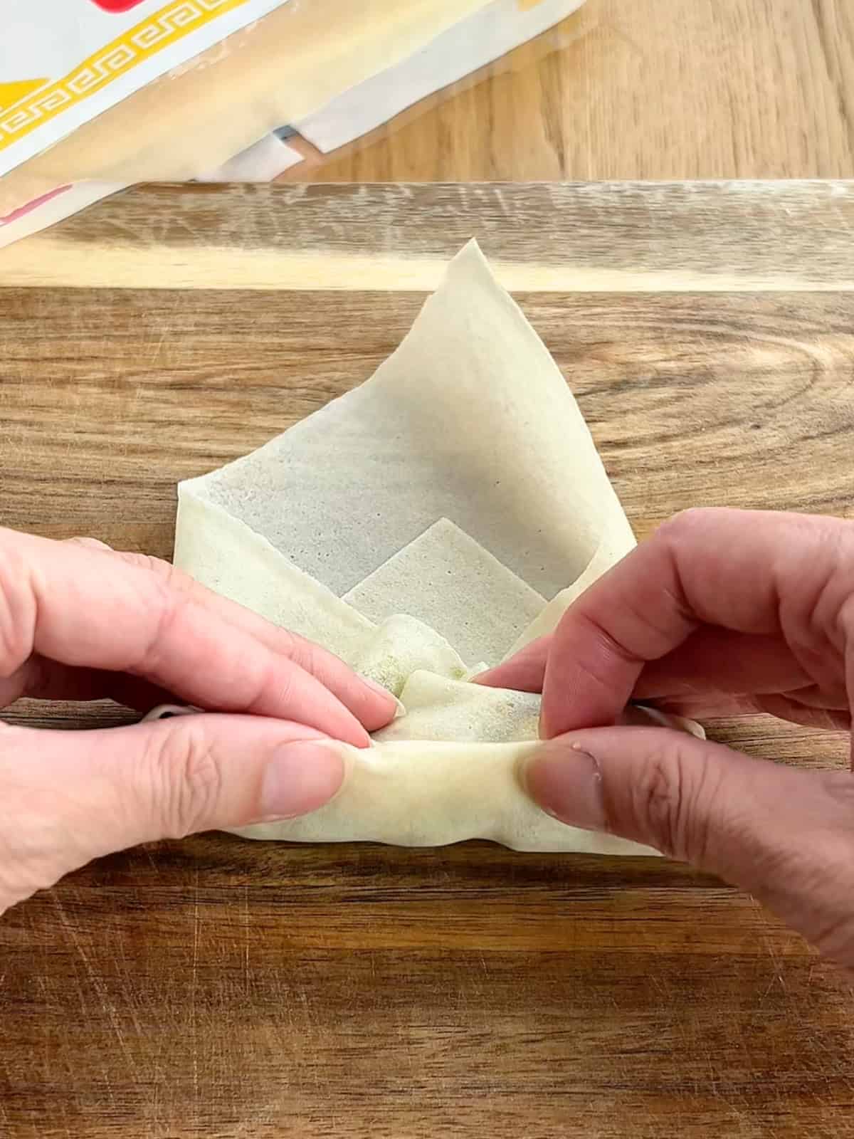 Two hands rolling up the egg roll on a wooden board.