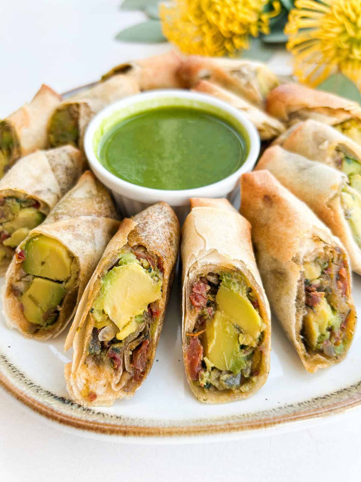 Side view of avocado egg rolls with a dipping sauce.