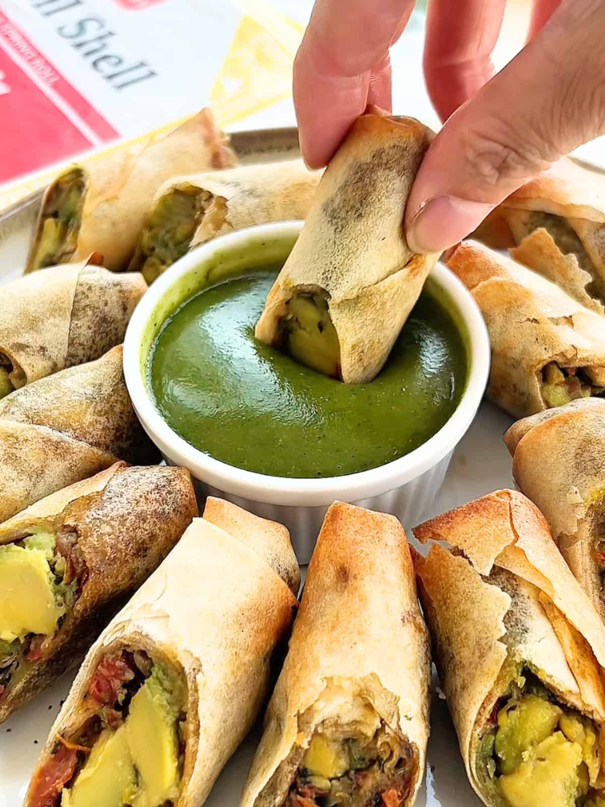 Hand dipping an avocado egg roll into the ramekin of sauce.
