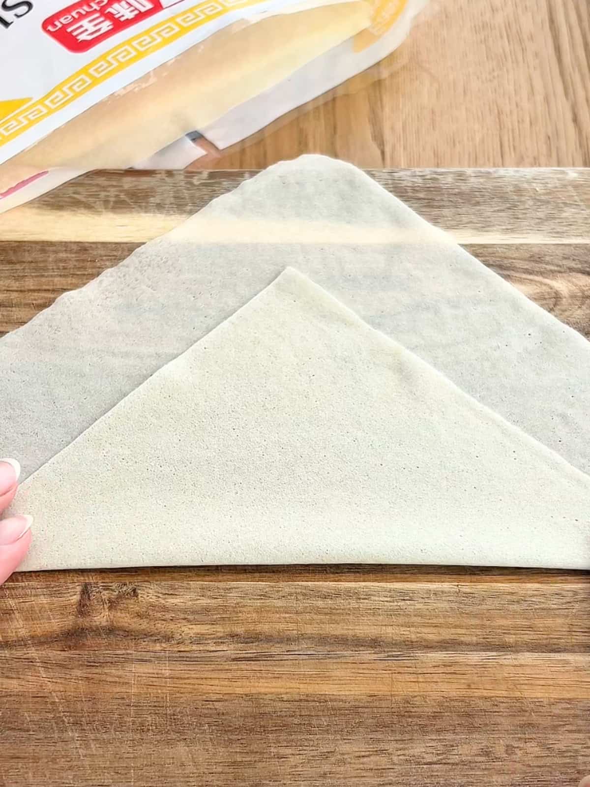 Folding the egg roll wrapper on a wooden board.