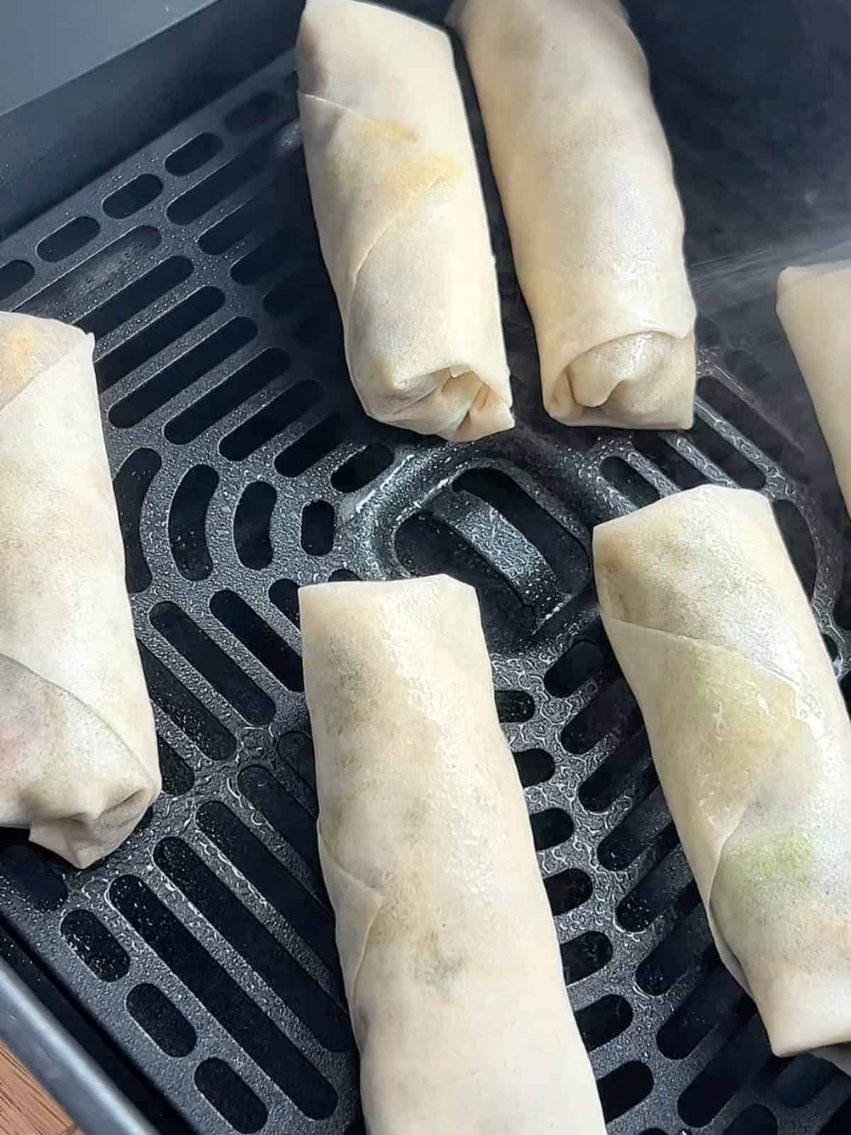 Placing the egg rolls in an air fryer basket.