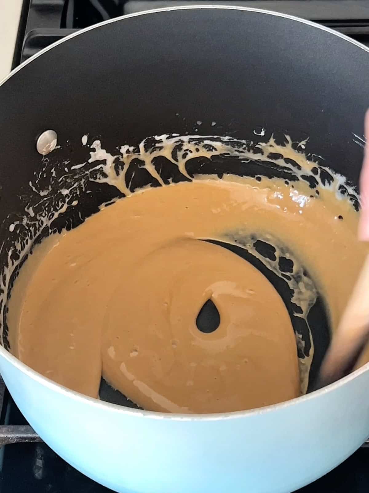 Stirring the fish sauce caramel into melted marshmallows in a pot.