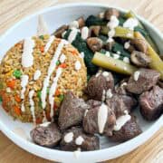 Close up shot of steak, veggies, fried rice in a bowl plate drizzled with yum yum sauce.