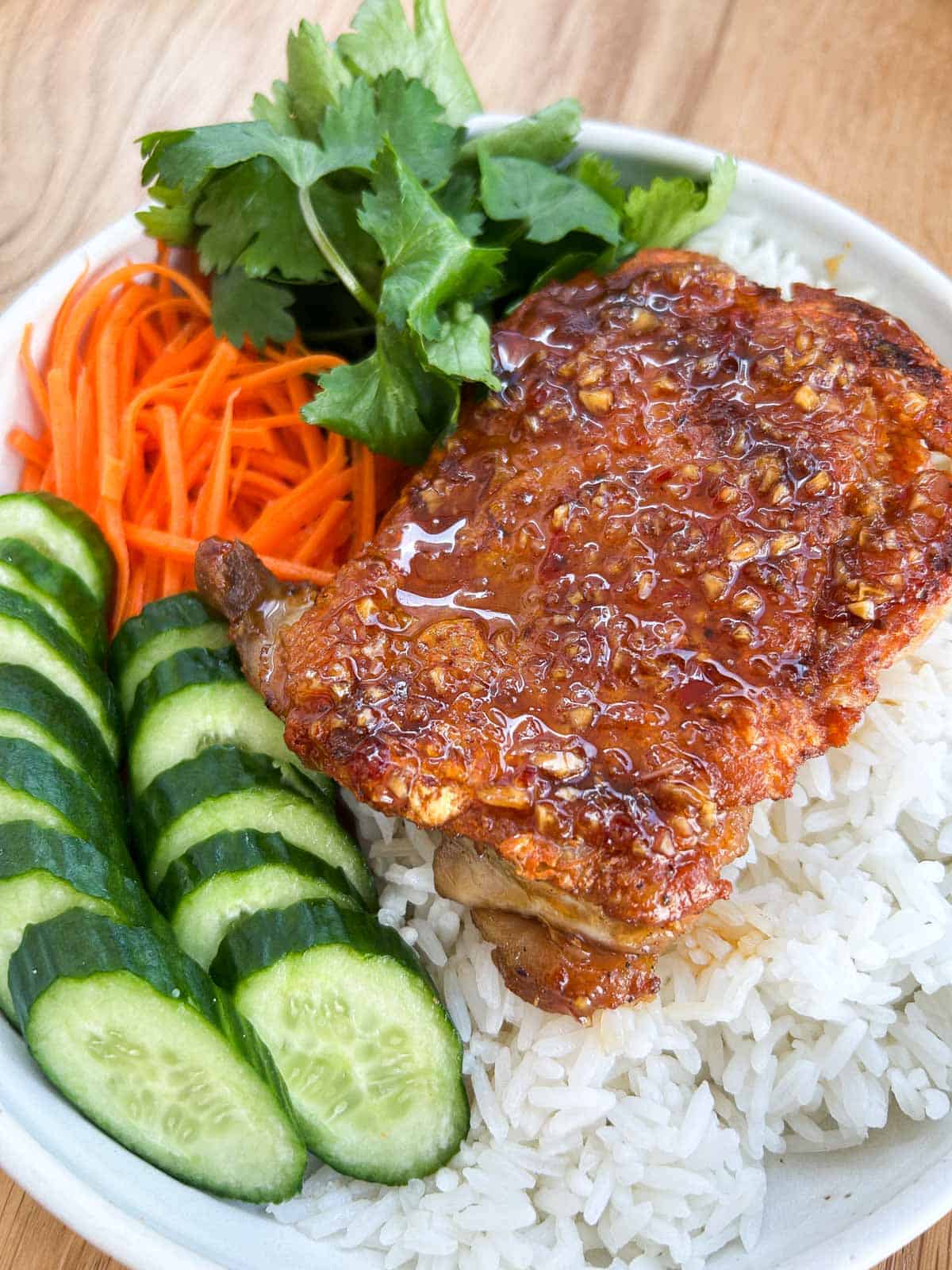 45 degree angled shot of crispy fish sauce glazed chicken thigh on a bed of rice with vegetables.