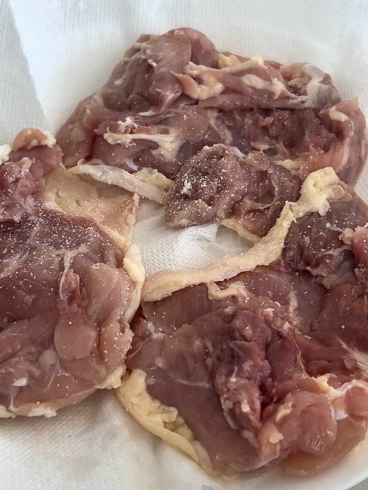 Three pieces of boneless skin on chicken thighs face down on a paper towel.