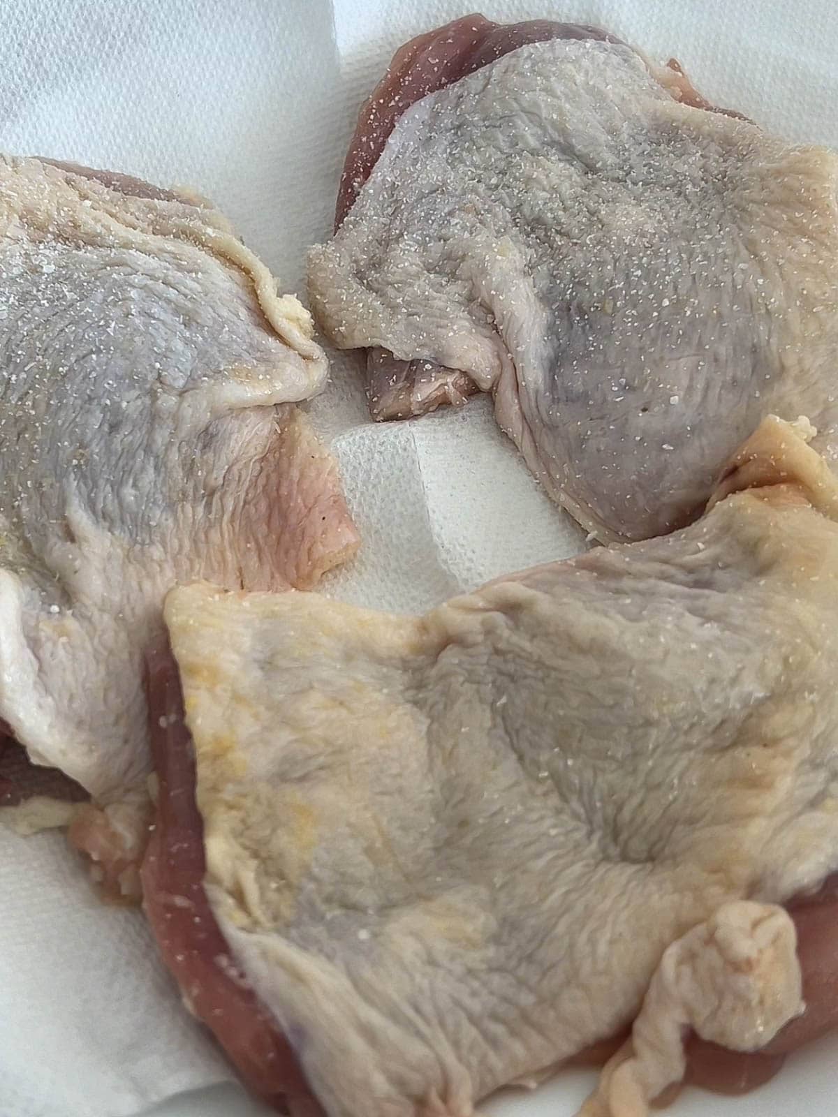 Three pieces of boneless skin on chicken thighs face up on a paper towel.