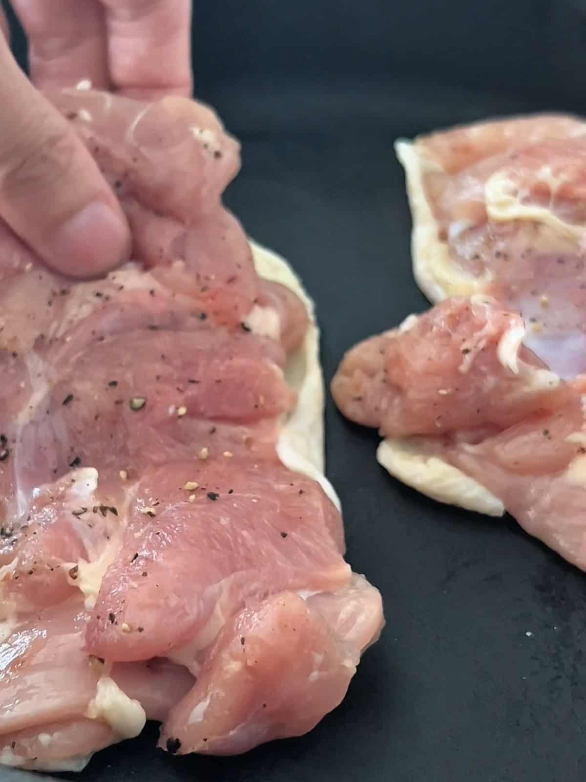 Two chicken thighs being placed skin side down in a pan.