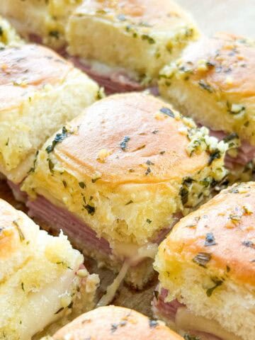 Side view of baked ham and cheese sliders with cheese pull.