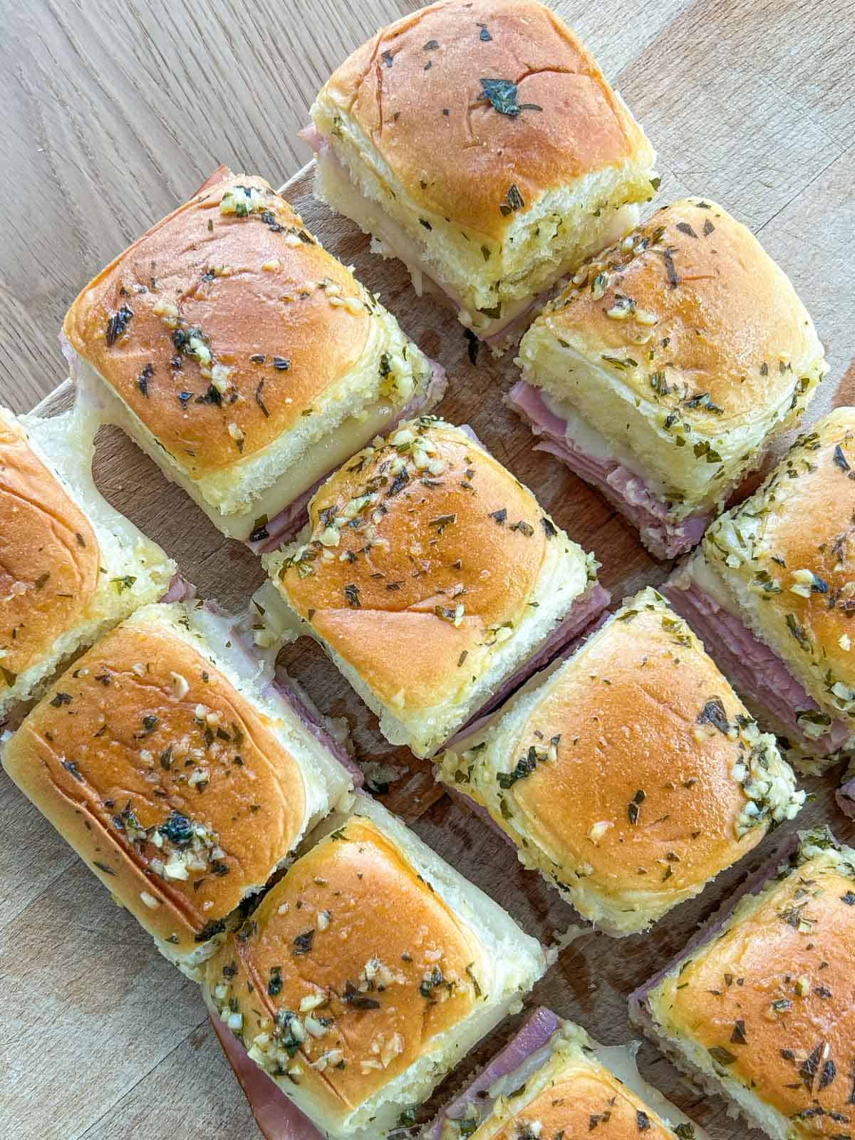 Cut ham and cheese sliders with cheese pull on a cutting board.