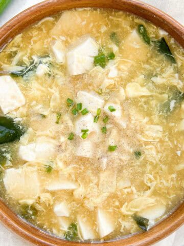 Miso egg drop soup in a bowl garnished with scallions and white pepper in a 1x1 photo.
