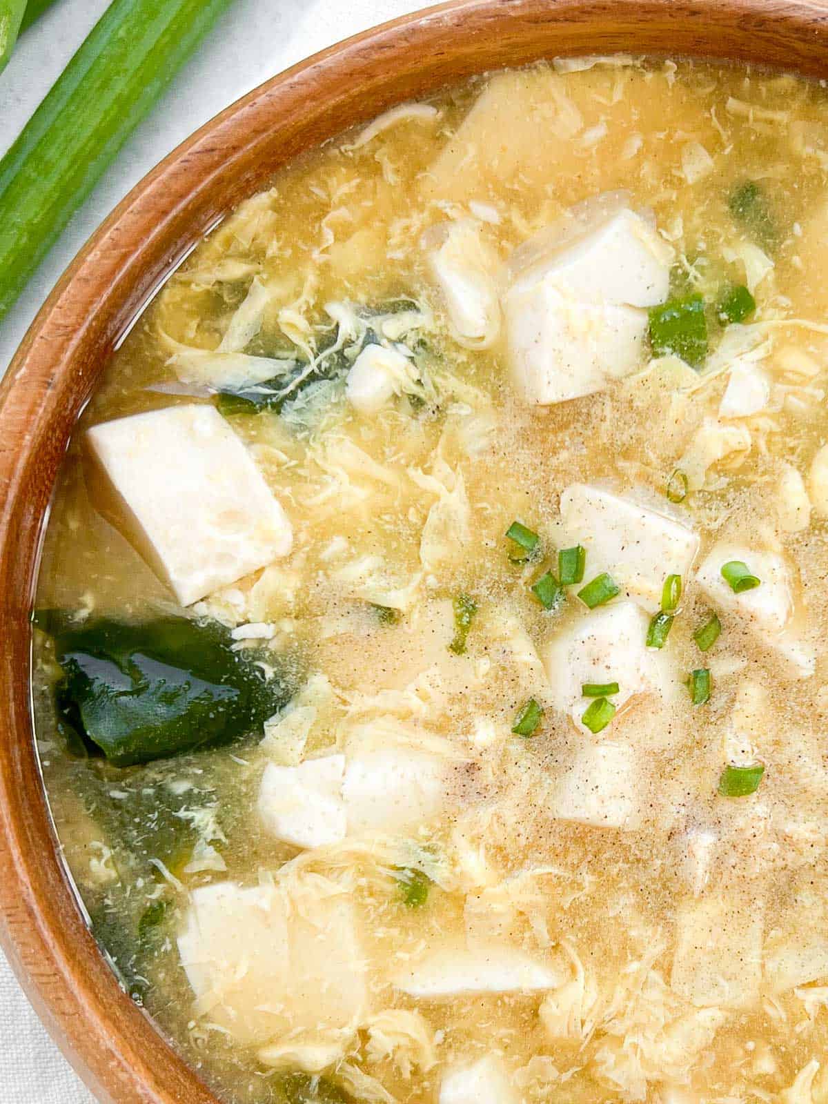 Close up corner shot of egg drop soup in a bowl garnished with scallions and white pepper.