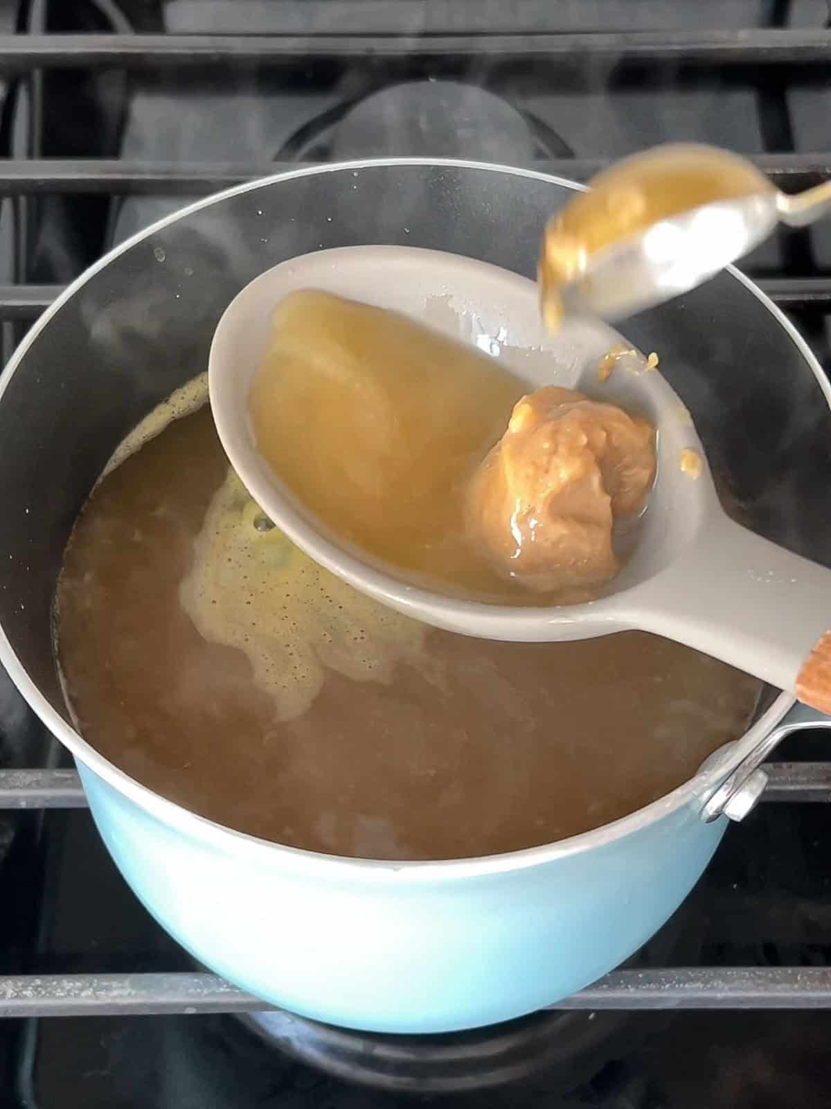 Miso paste being dissolved in a ladle with some broth over a pot.