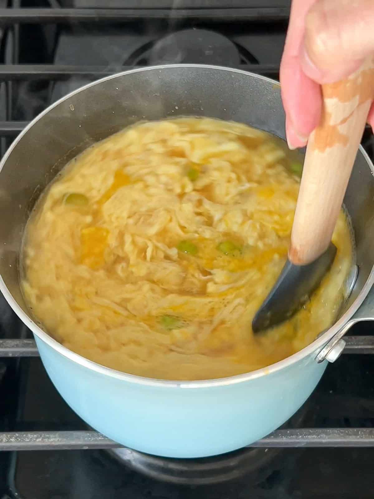Egg ribbons being stirred in a pot of soup.