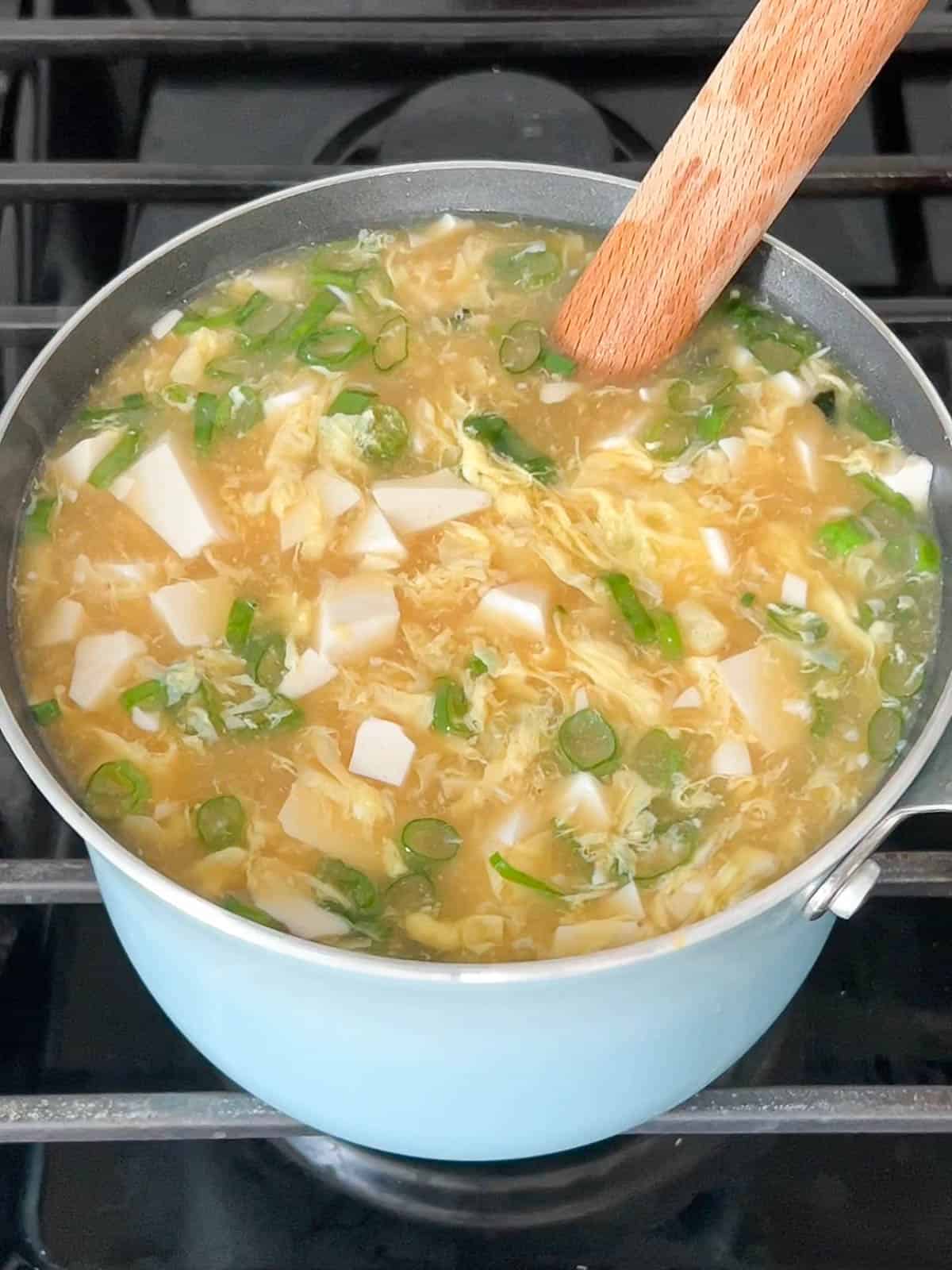 Miso egg drop tofu soup in a pot garnished with scallions.