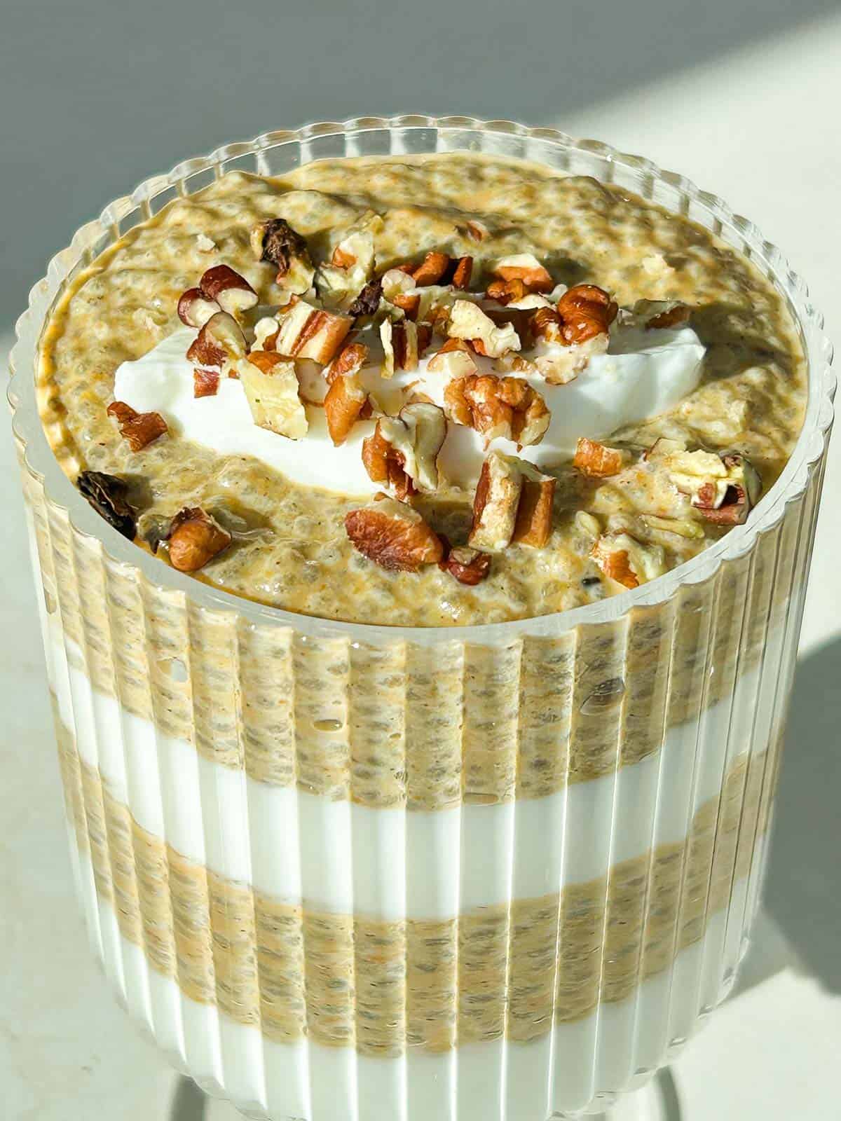 A longer photo of the close up angle of pumpkin chia pudding topped with greek yogurt and chopped pecans.