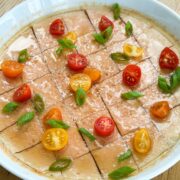 Close up shot of steamed egg with tomato garnished with scallions, cut baby tomatoes, soy sauce, and sesame oil.