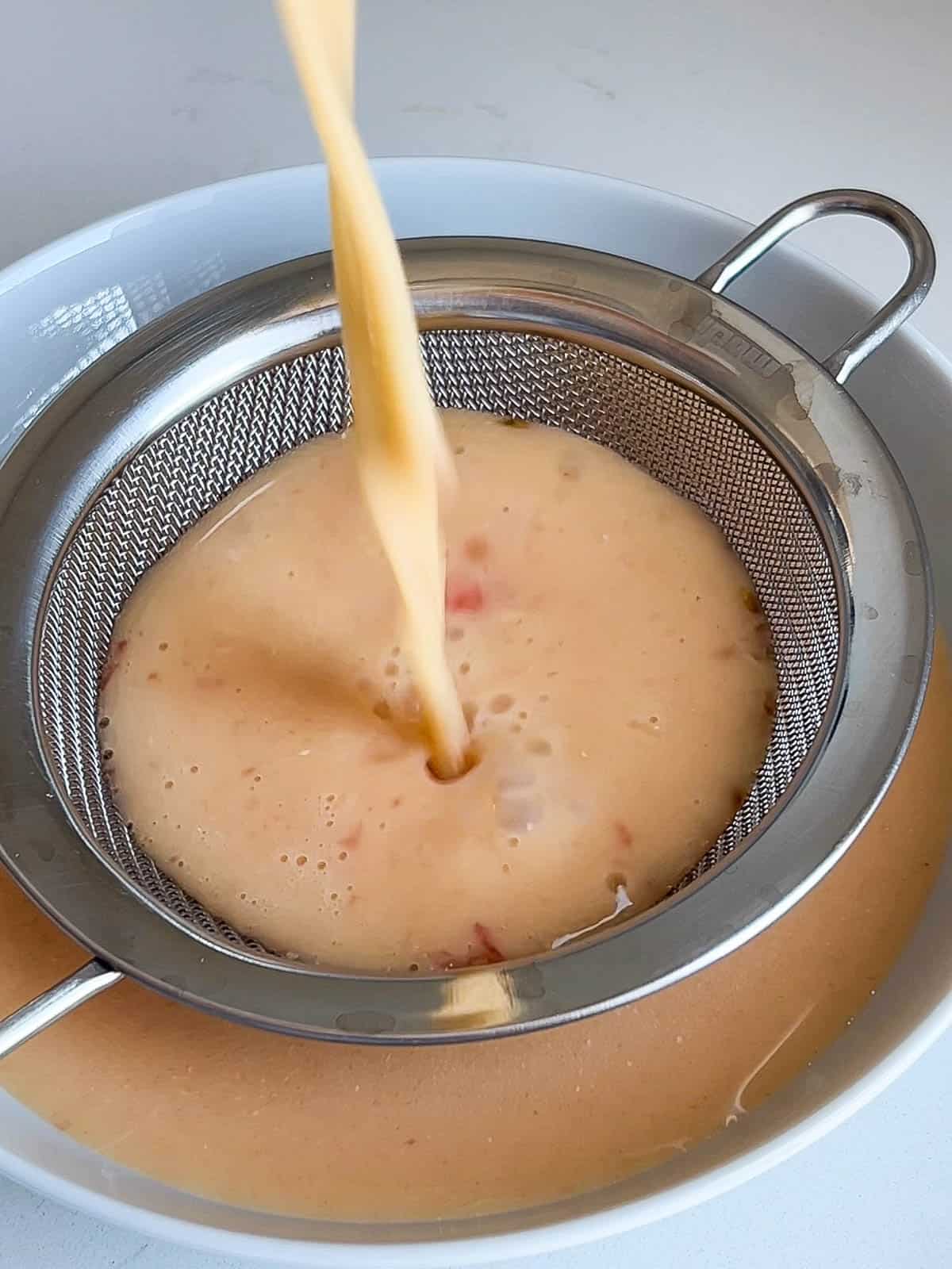Egg mixture poured through a sieve into a bowl.