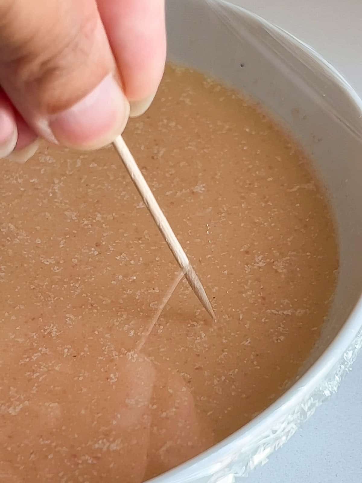 Egg mixture in a dish with saran wrap over it and toothpick pricking holes.