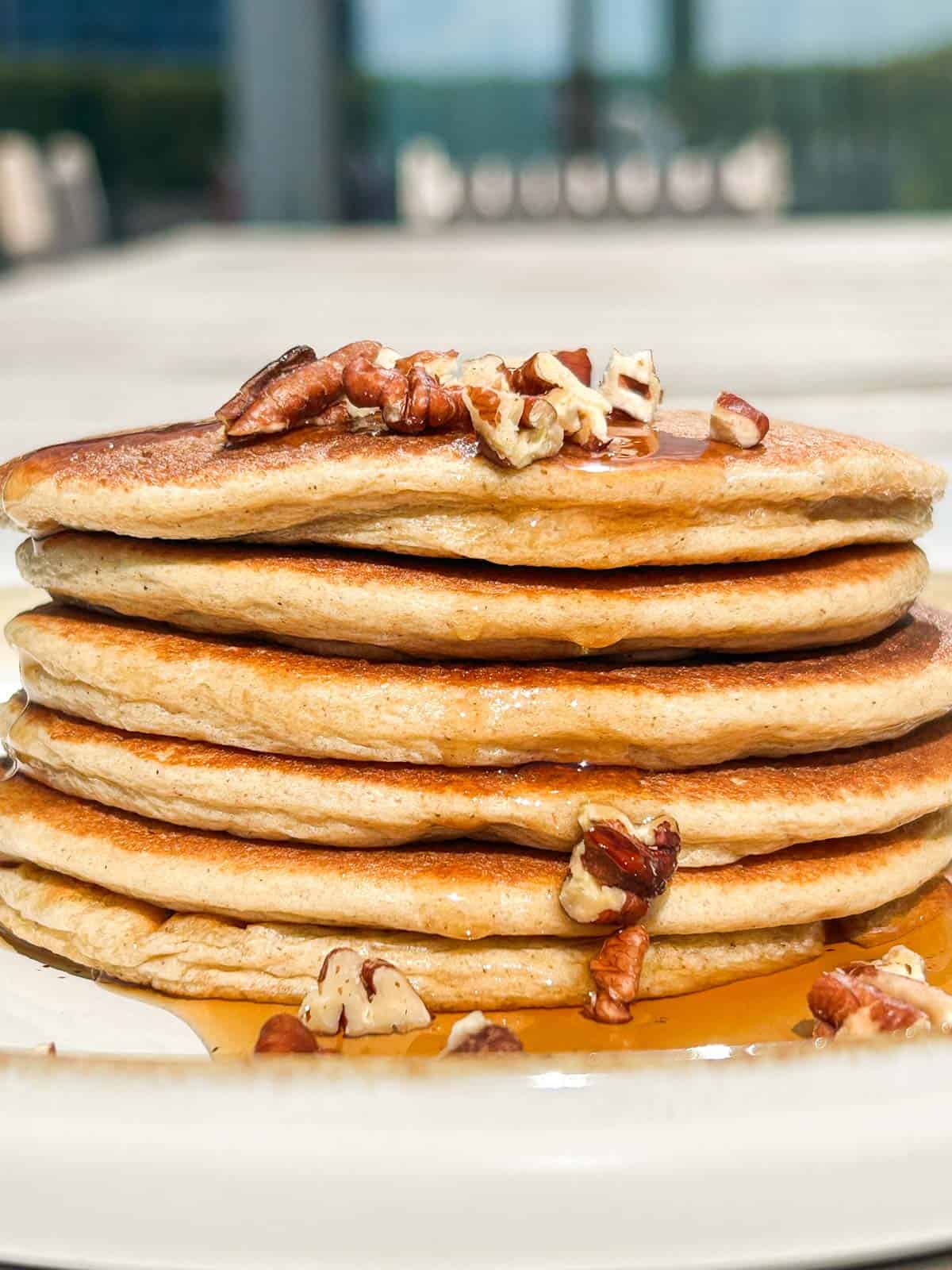 Side shot of stack of pancakes with pecan pieces on top and maple syrup dripping down the side but longer shot.