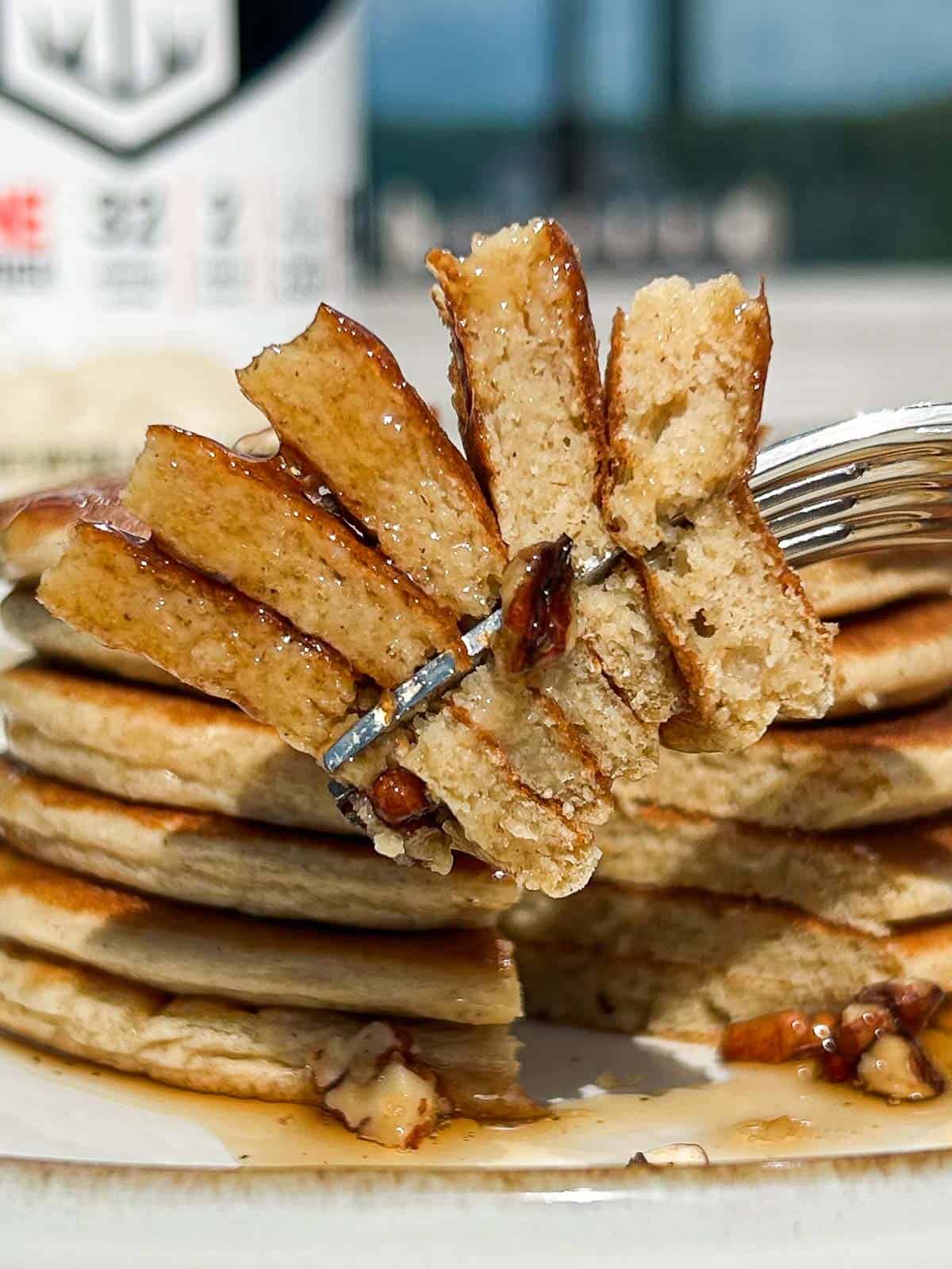 Side shot of cut pancakes on a fork with maple syrup dripping down.