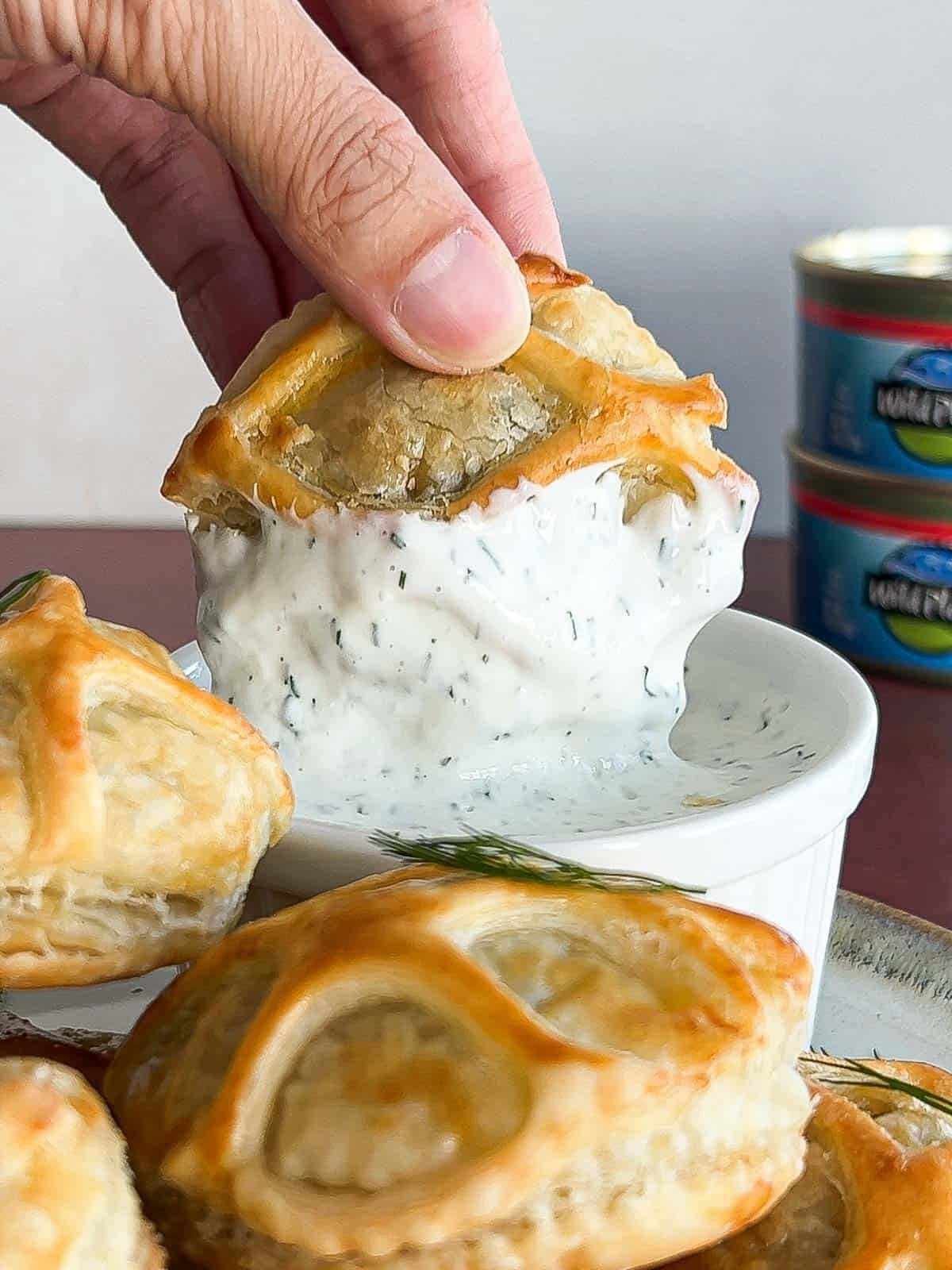 Finished salmon wellington pastry being dipped in the creamy dill dipping sauce.