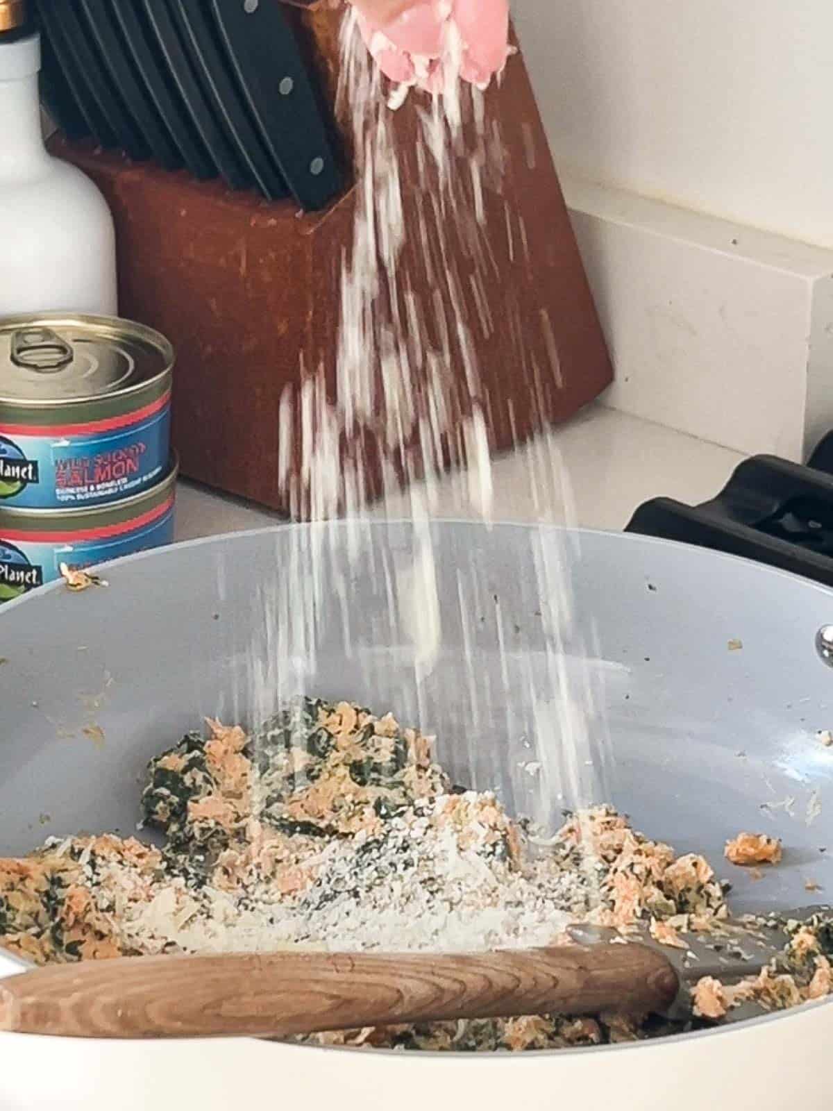 Salmon filling in a pan being sprinkled with parmesan cheese.