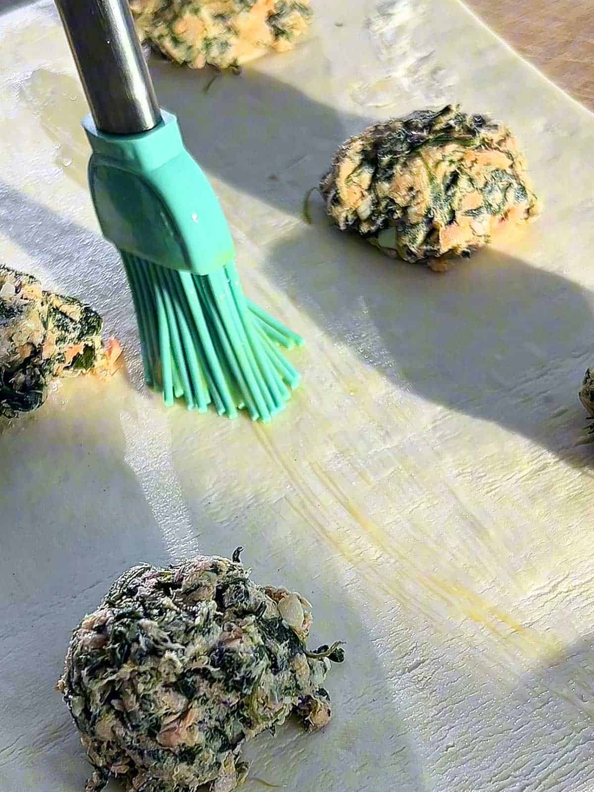 Tablespoons of salmon filling on puff pastry with egg wash brushed around.