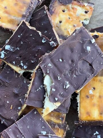 Finished and cooled saltine cracker toffee covered in chocolate broken up in a pile on a sheet pan in a 1x1 format.
