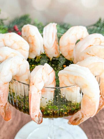 Close up shot of shrimp cocktail hanging around the rim of a coupe glass with dipping sauce inside.