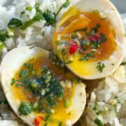 Up close jammy soft boiled eggs cut in half on a bed of rice, drizzled with cilantro fish sauce.
