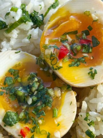 Up close jammy soft boiled eggs cut in half on a bed of rice, drizzled with cilantro fish sauce.